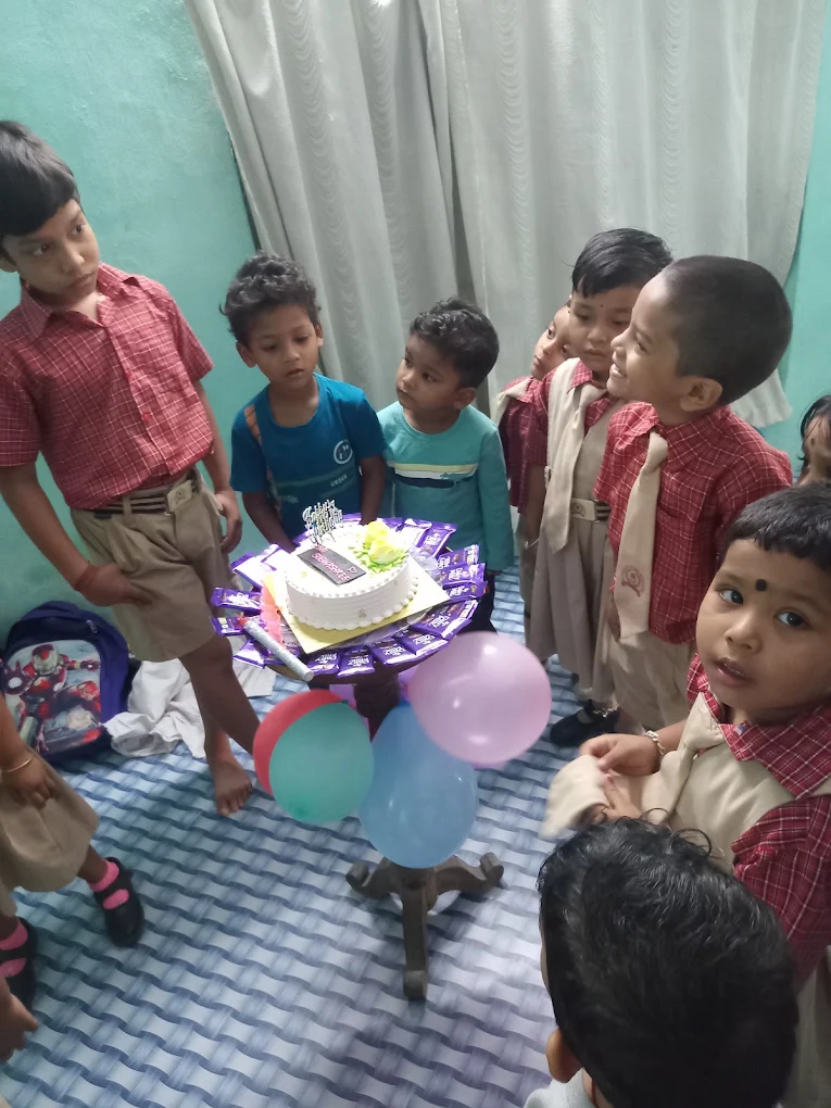 Children gathered around a birthday cake and balloons in a school room